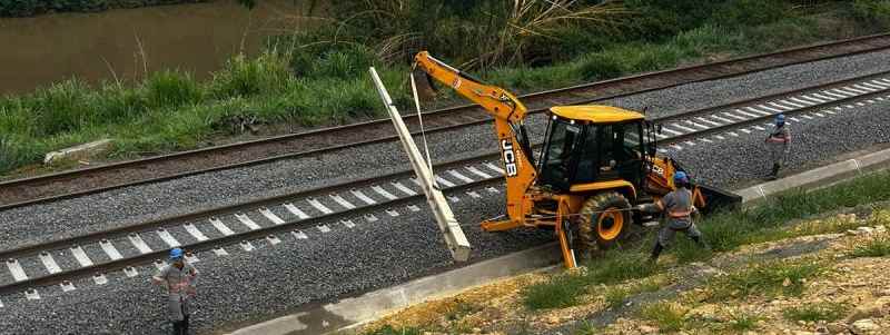 Tratotor levantando poste elétrico em linha ferroviária